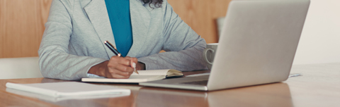 businesswoman writing in a notebook in front of her laptop.